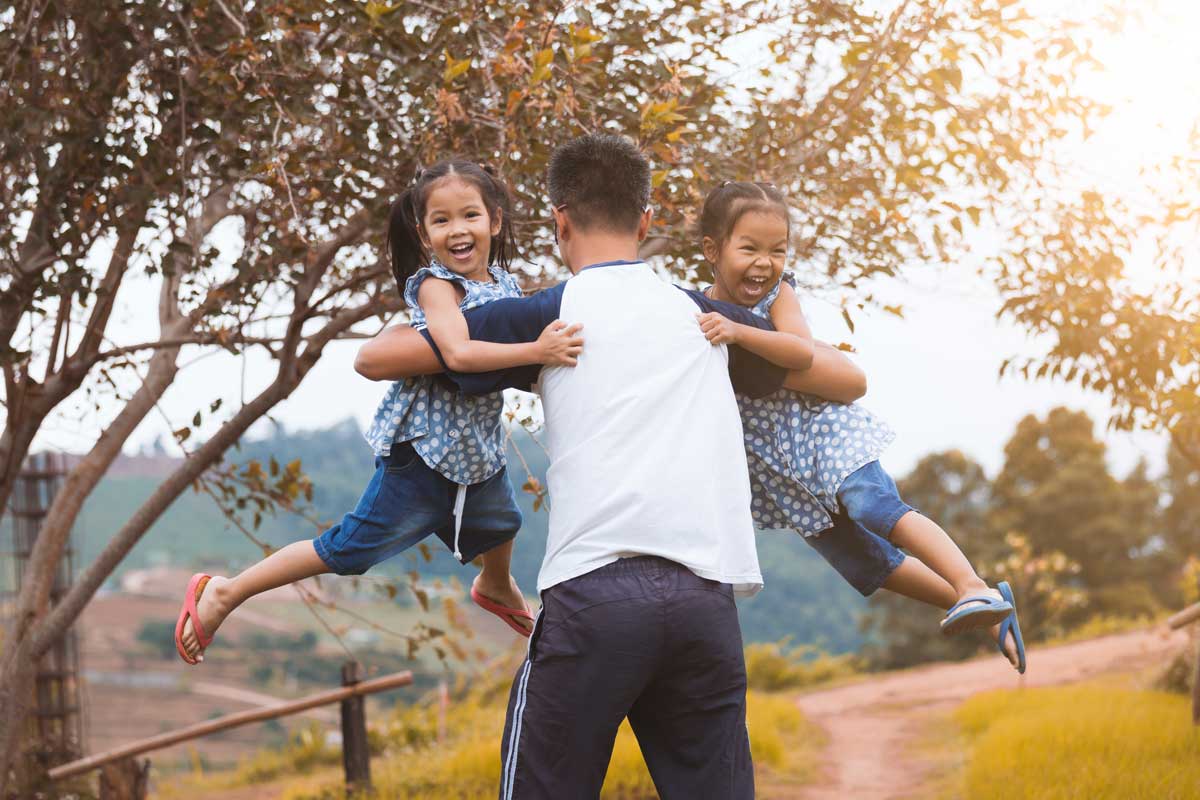father carrying and playing his two twin daughters on international youth day
