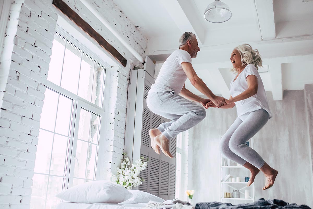 An elderly couple jumping on a bed