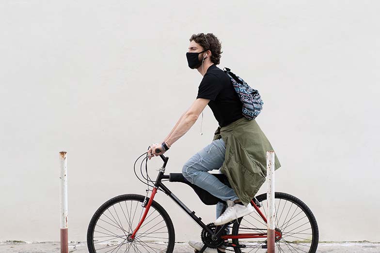 Young man riding his bike stress free and wearing a mask amid COVID-19 pandemic