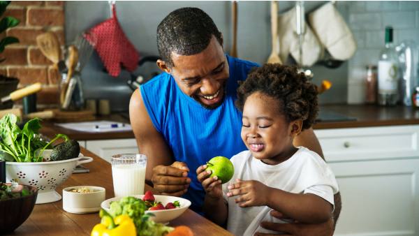 man in blue shirt in kitchen with daughter eating fruit