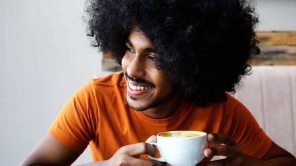 man in orange shirt and curly hair with coffee