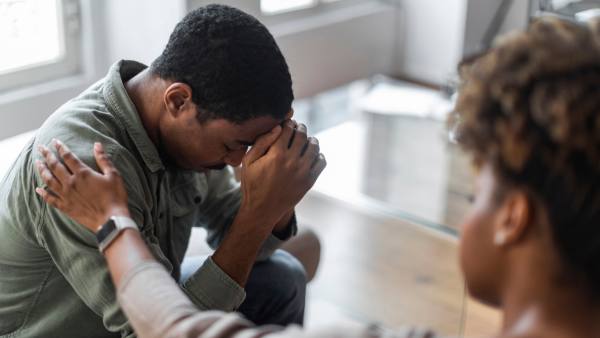 man with his head in his hands being comforted by a woman
