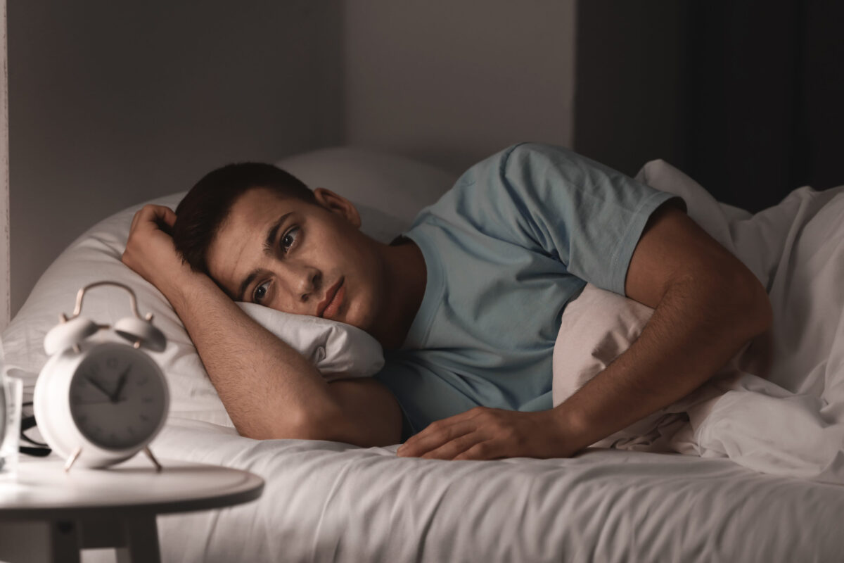 Young man in bed unable to sleep staring at clock