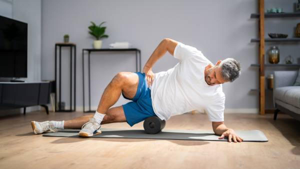 man with grey hair using foam roller on floor