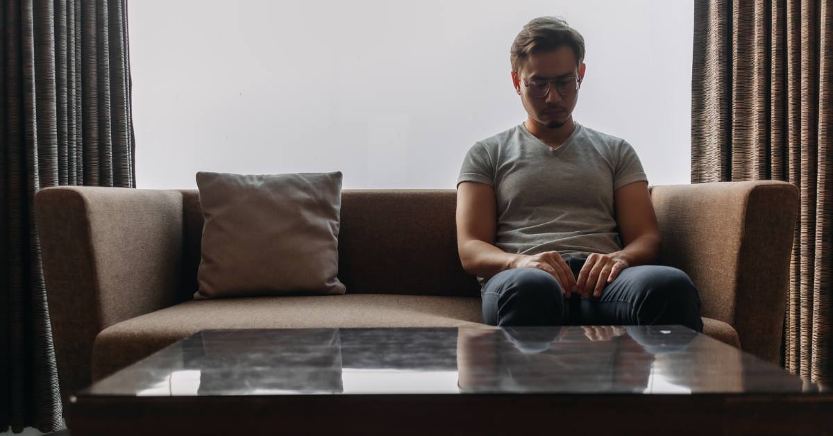 Lonely asian man sits on the sofa grieving