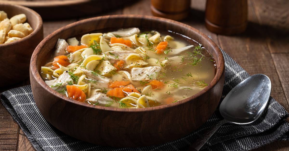 wooden bowl of chicken noodle soup with spoon on a napkin