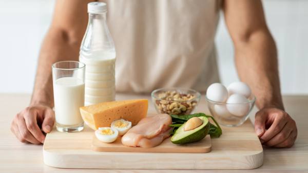 wooden cutting board with chicken, eggs, milk, avocado, and nuts with man's arms
