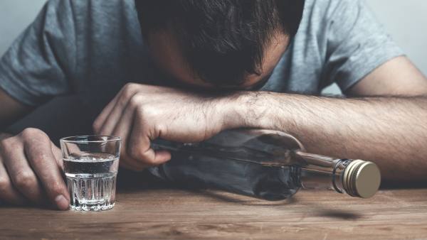man with his head on a table hugging empty alcohol bottle and with a shot glass