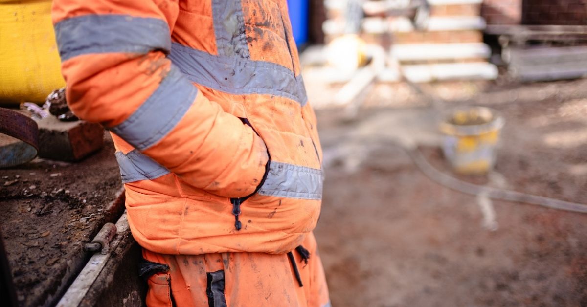 man in dirty orange work clothes leaning on vehicle